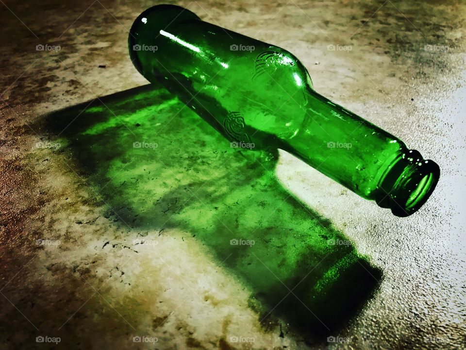 Light through a green glass beer bottle on a textured kitchen floor. Contrasty colorful bottle casting a cool green shadow. 