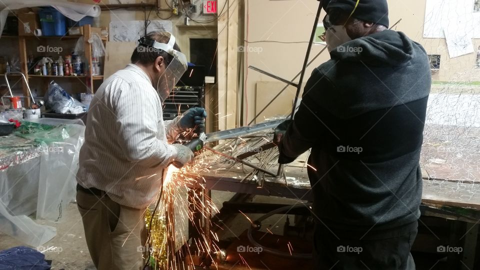 man grinding the metal frame and other person holding the frame