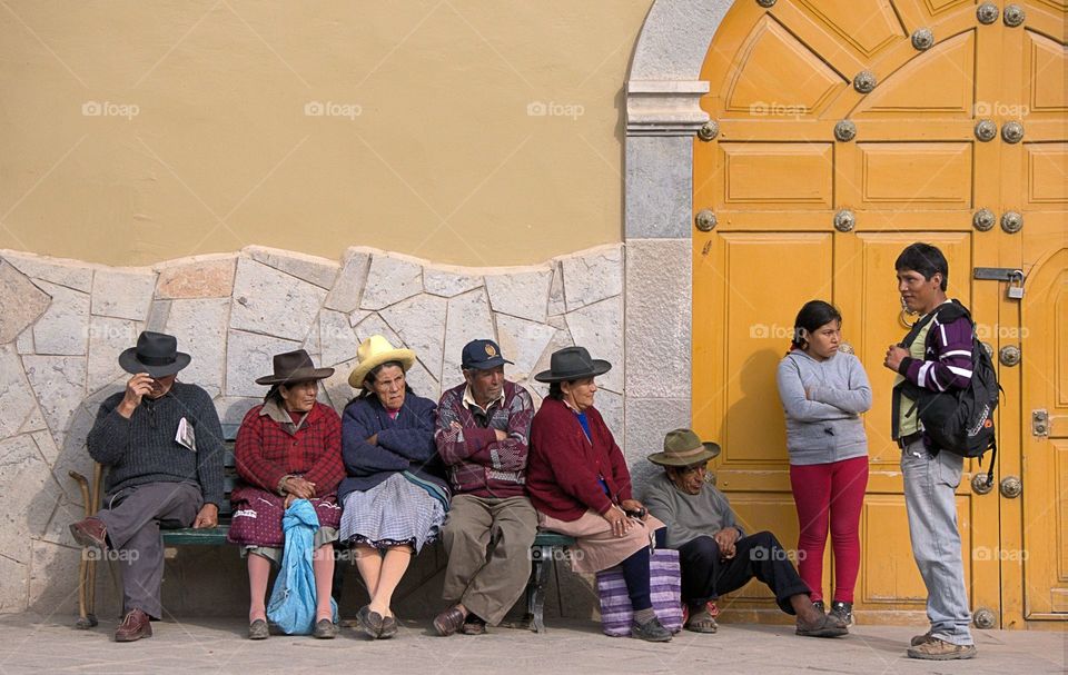 Several local people are seated and standing waiting for the church across from the main plaza in Ollanraytamvo, Peru to open,