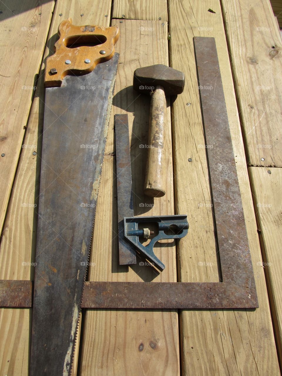 Carpenters hand tools, mallet, hand saw, squares & level. Layout on decking, outdoors.