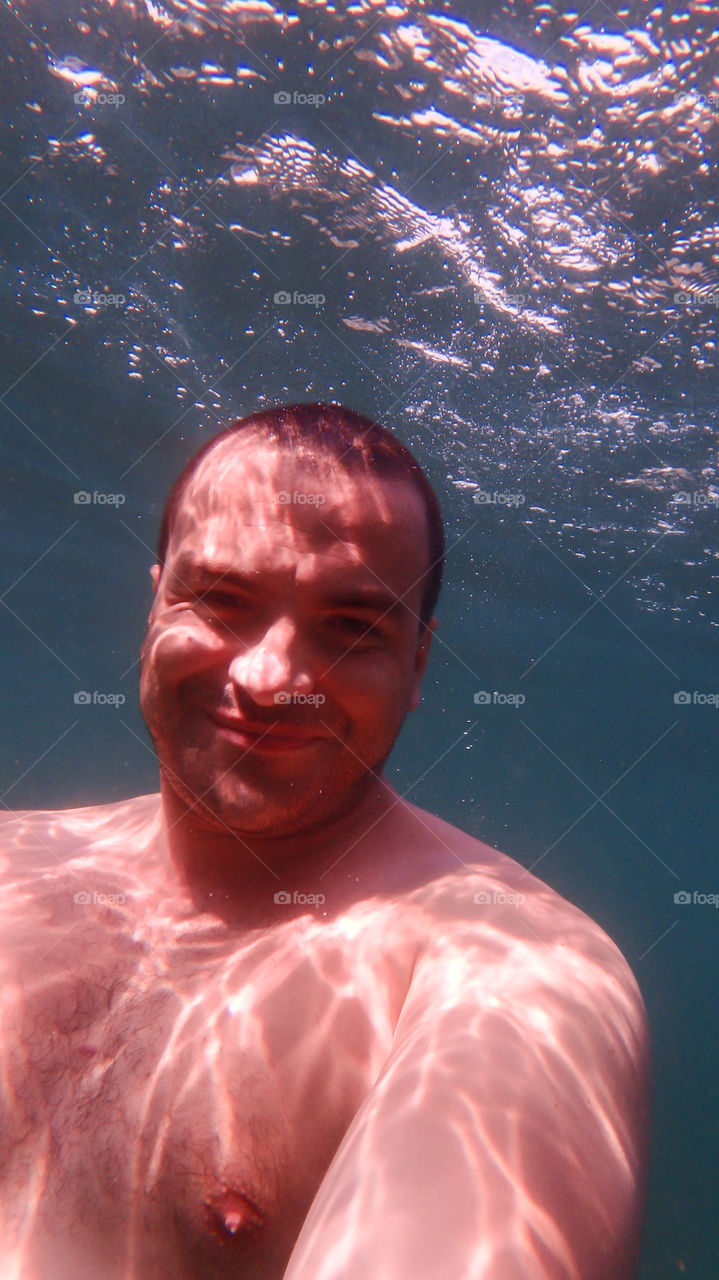 Man diving, man underwater smiling and relaxing in big blue sea with his camera