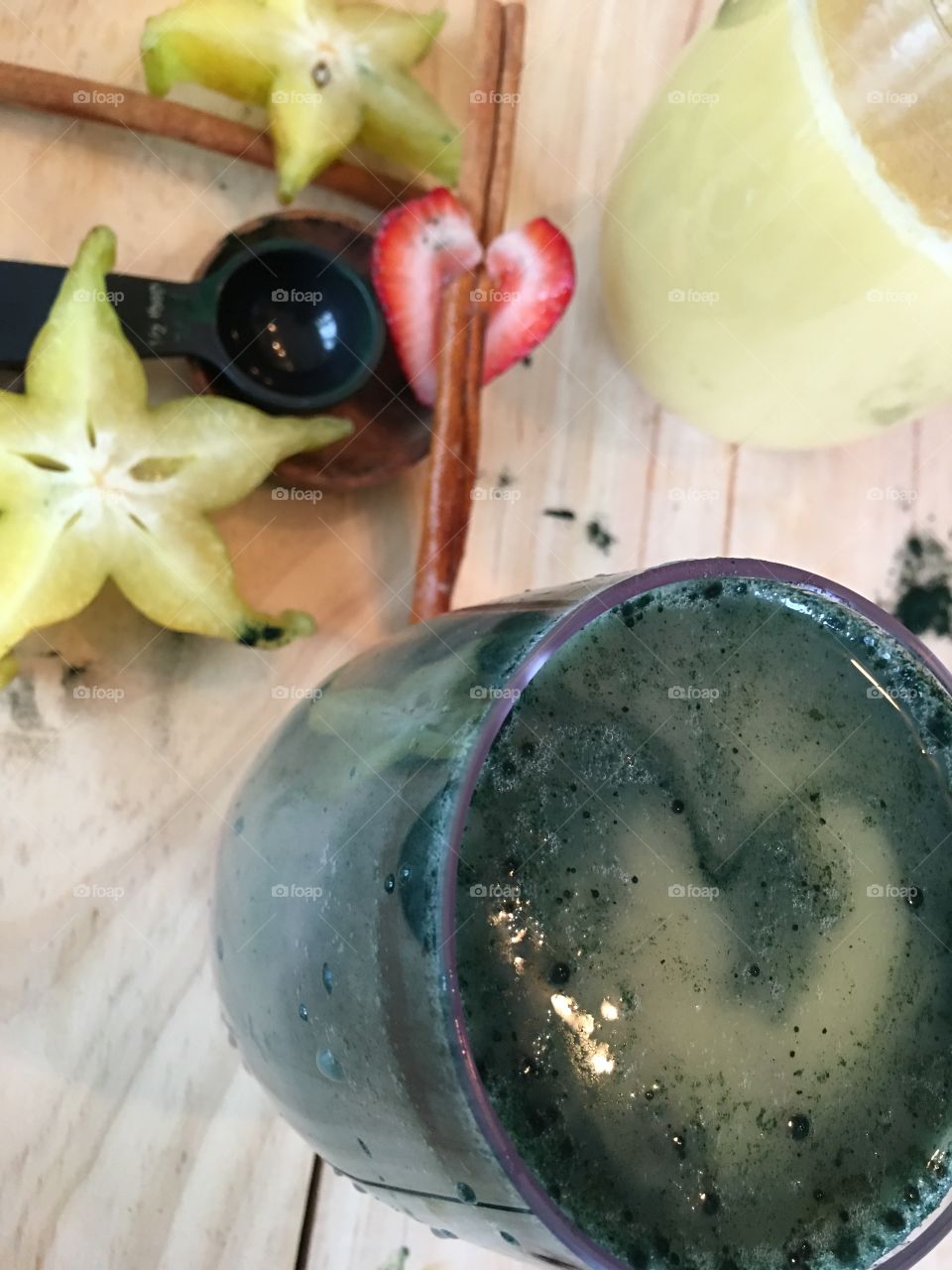 High angle view of green mixed tropical fruit smoothie with spiroulina powder strawberry, coconut, banana squirls in colorful layers with star fruit and cinnamon sticks 