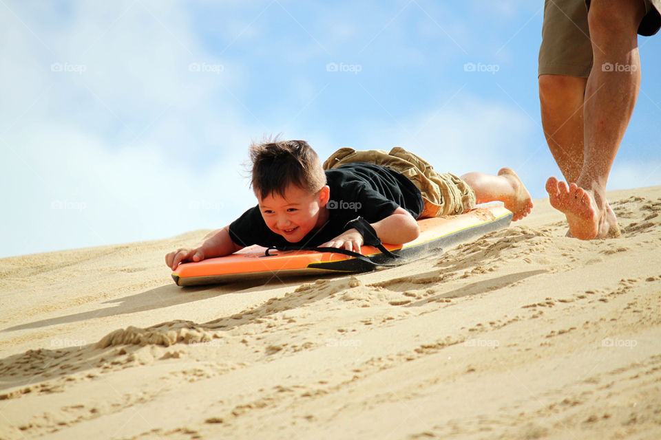 A little boy sliding a board on sand dunes