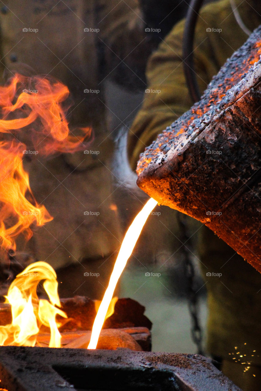 Steelworker pours molten iron into molds