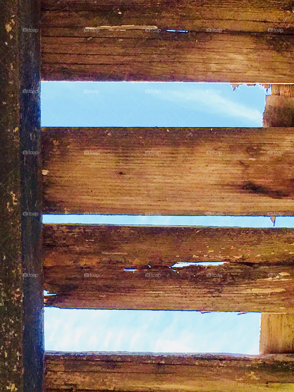 A view of bright blue sky seen through the wooden rafters of an old, weather-beaten structure