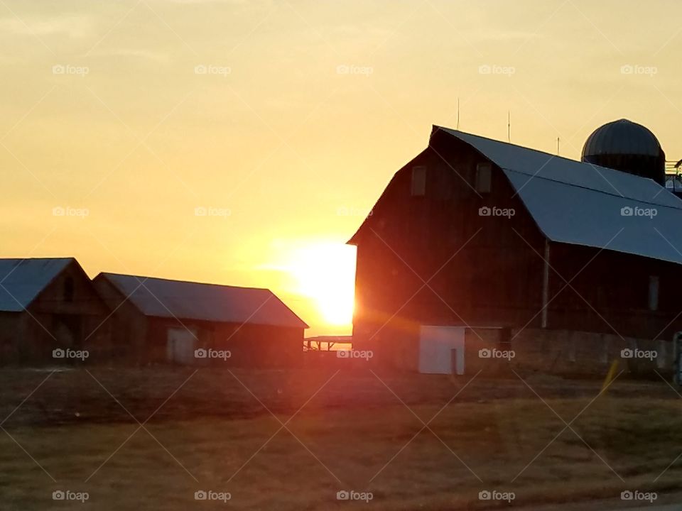 The light shines trough. 
The sunset as it lowers between the farm buildings