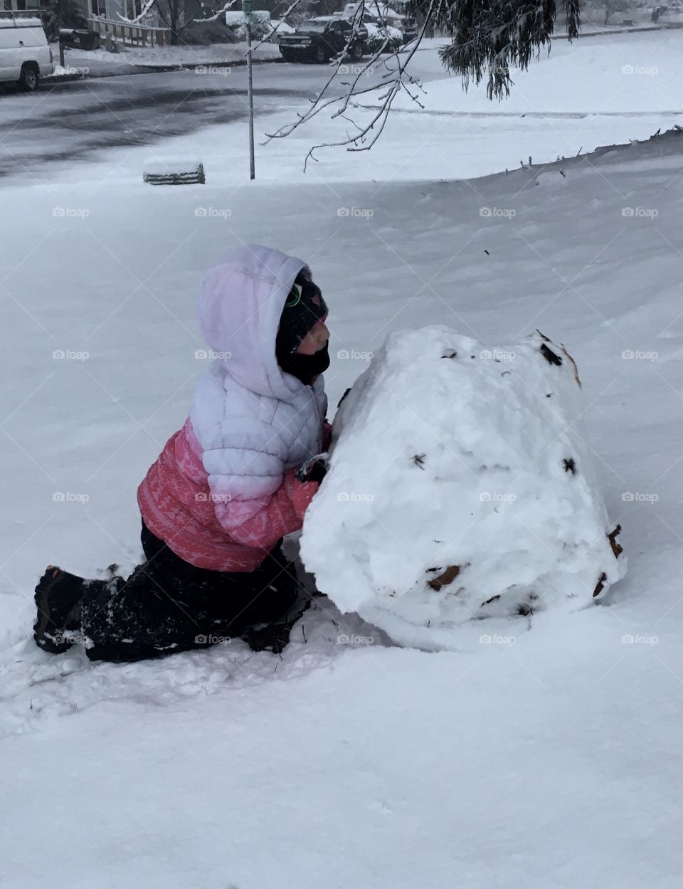 Child rolling a huge snowball up a hill