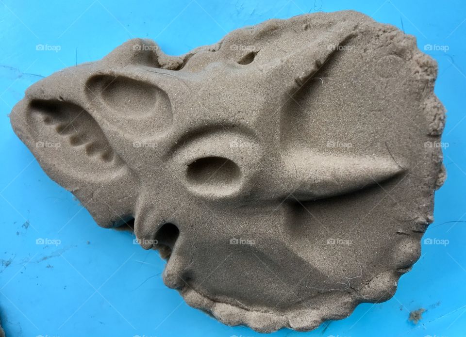 Close up sand sculpture of a triceratops dinosaur skull on a blue background. Lines and details. 