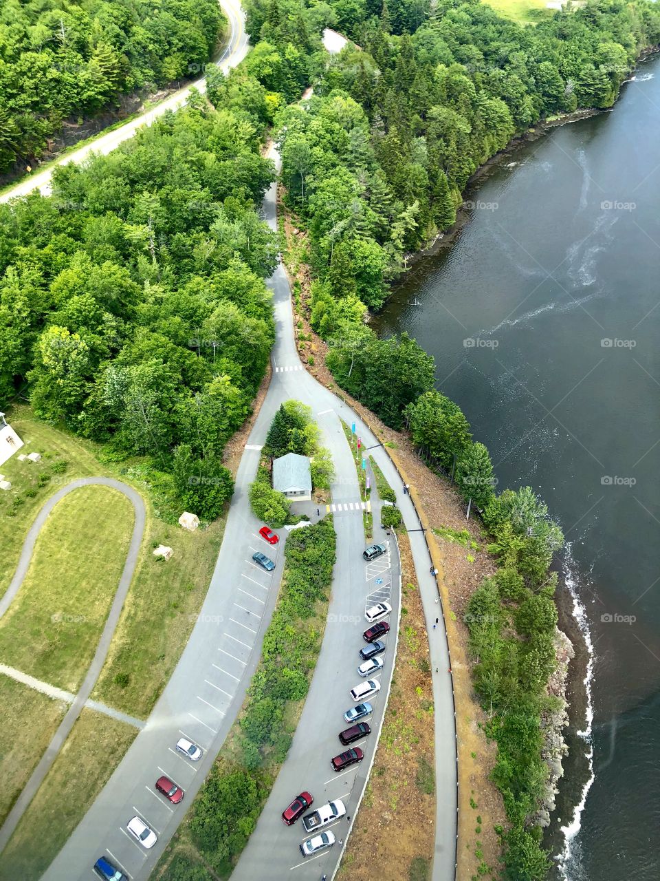 Scenic aerial view of Penobscot Bay and surrounding coastline from top of Penobscot Narrows Bridge Observatory Tower, the largest bridge observation tower in the world. Landscape is covered with green grass, water, road and trees.