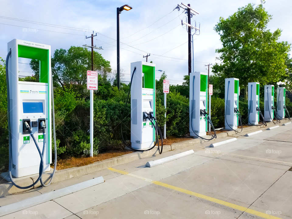 EV station- Green and white EV pumps with green shrubs in the background.