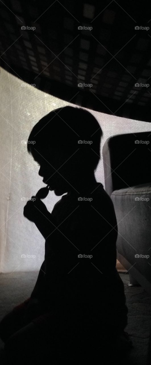 Pop fun. Silhouette of a boy eating a Popsicle in his home made fort.