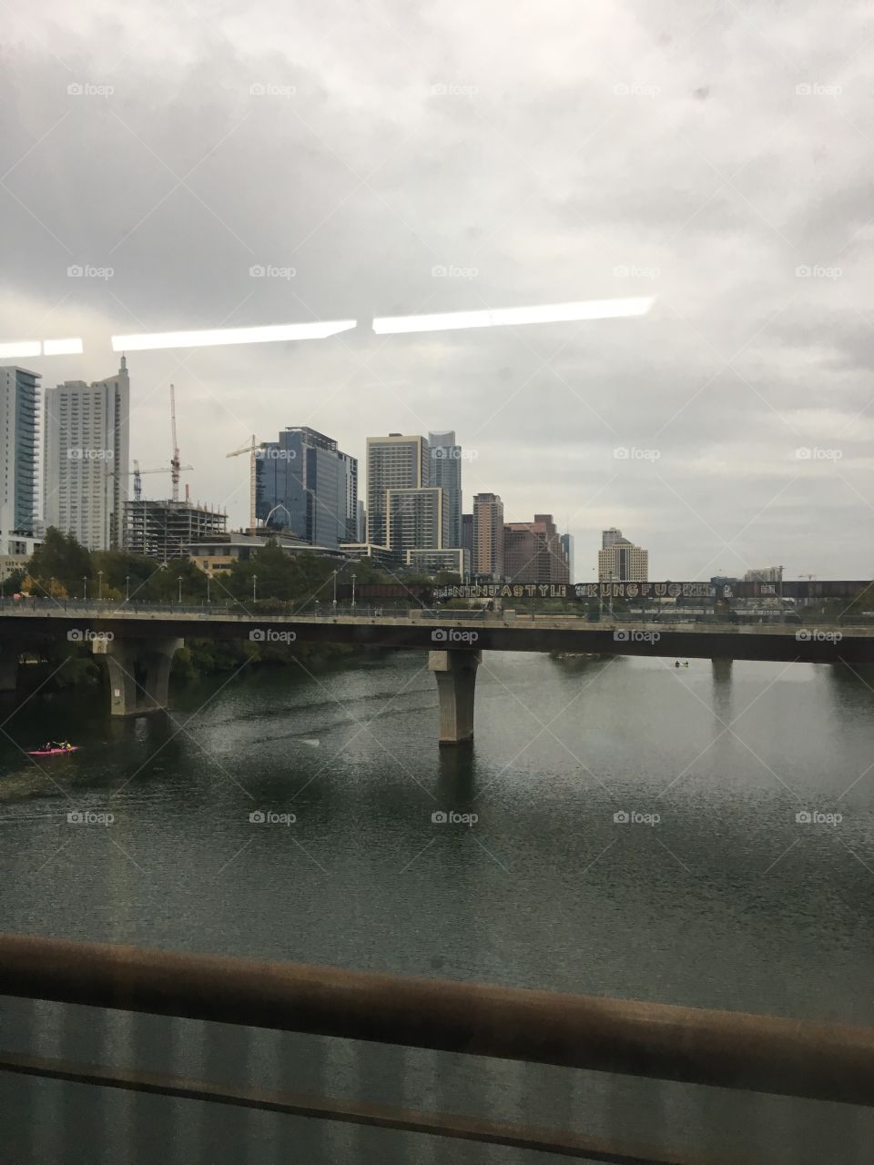 bridge over a River by the city on a rainy day in Austin with a bit of a glare from the bus light 