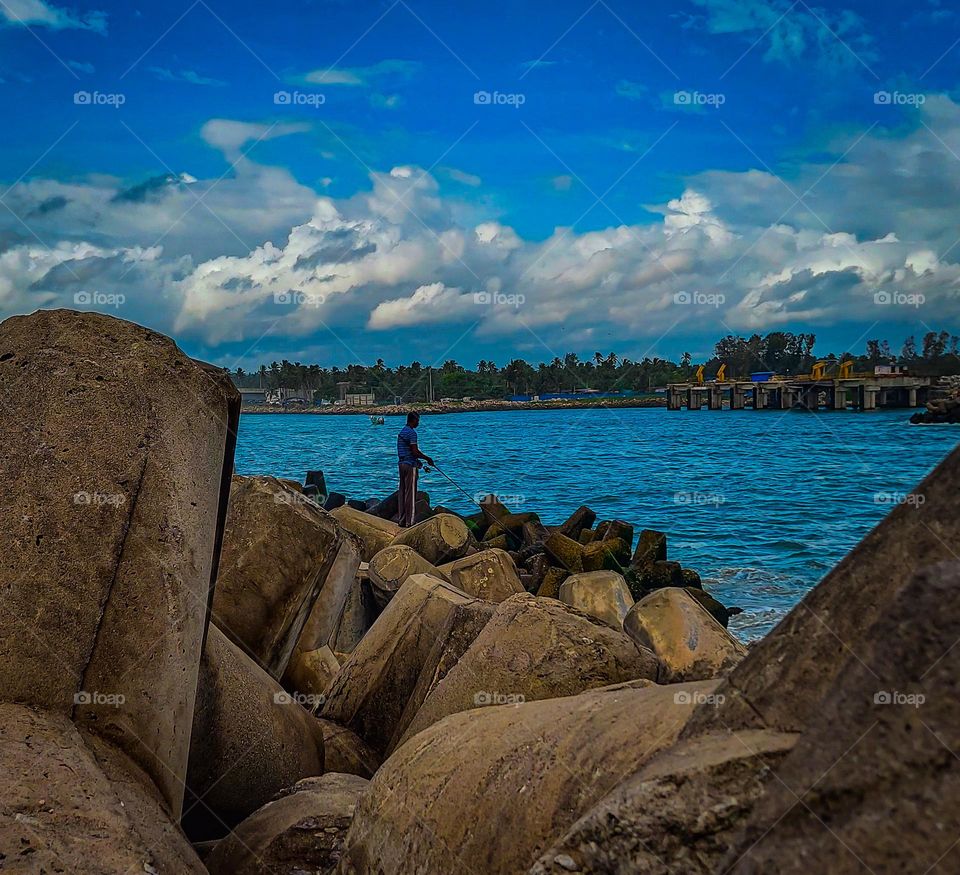 A fishermen fishing from sea under blue sky using traditional fishing method