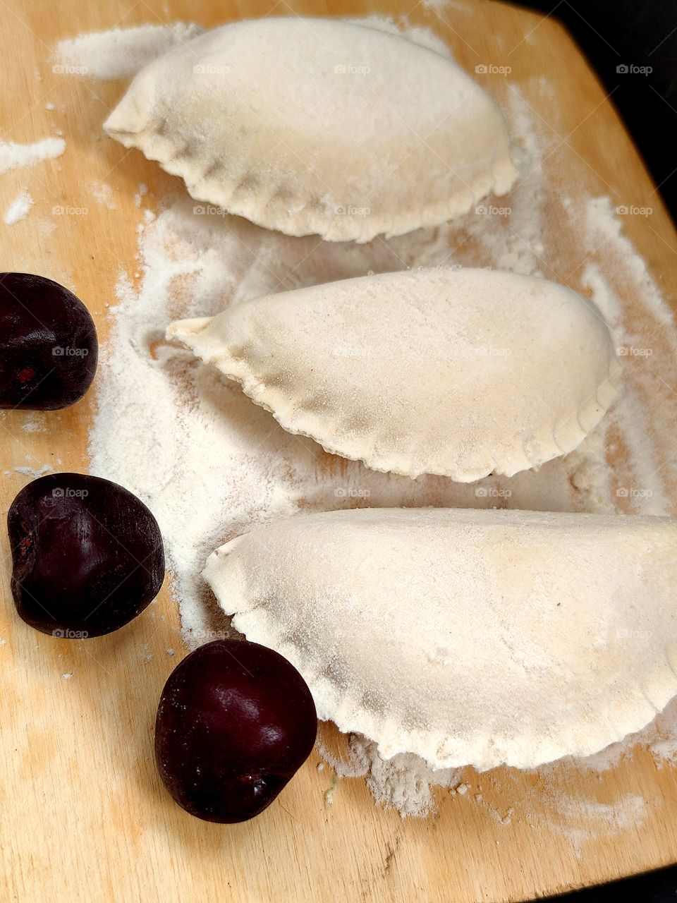 dumplings on a wooden board in flour.  Cherry.  Black background