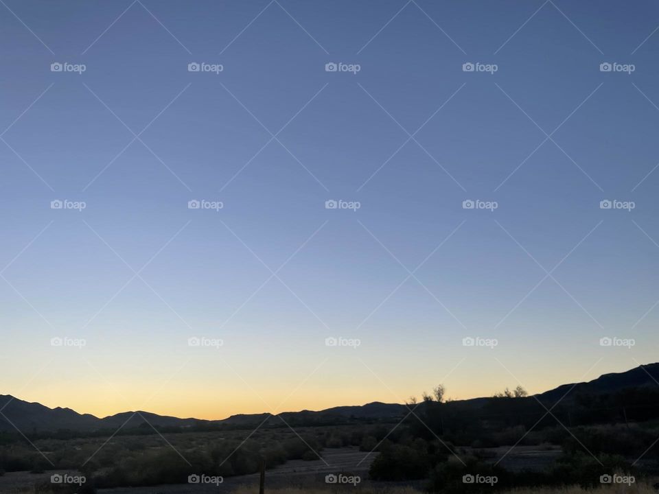  A yellow sunset with mountains and some trees. 