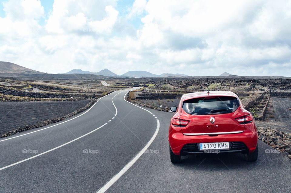 Red car parked alongside a long winding road on Lanzarote. The road crosses a vast volcanic valley.