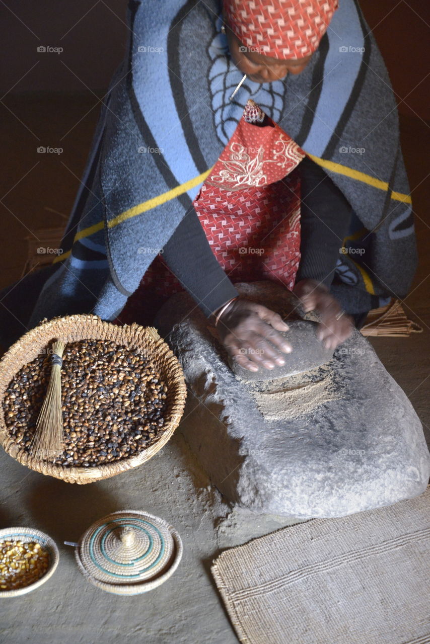A traditional Basotho gogo (grandmother ) that is showing us how she is crushing Sorghum and corn by using a rock. The produce is used to eat as porridge or used to make a traditional beer.