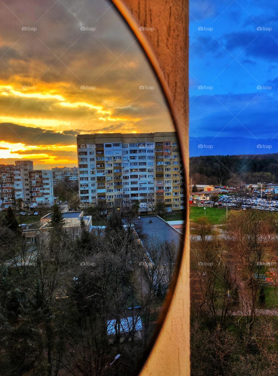 A photo of a colourful sunset reflection in a mirror in the capital of Bulgaria with bright yellow and orange sky in the reflection and blue skys on the other side