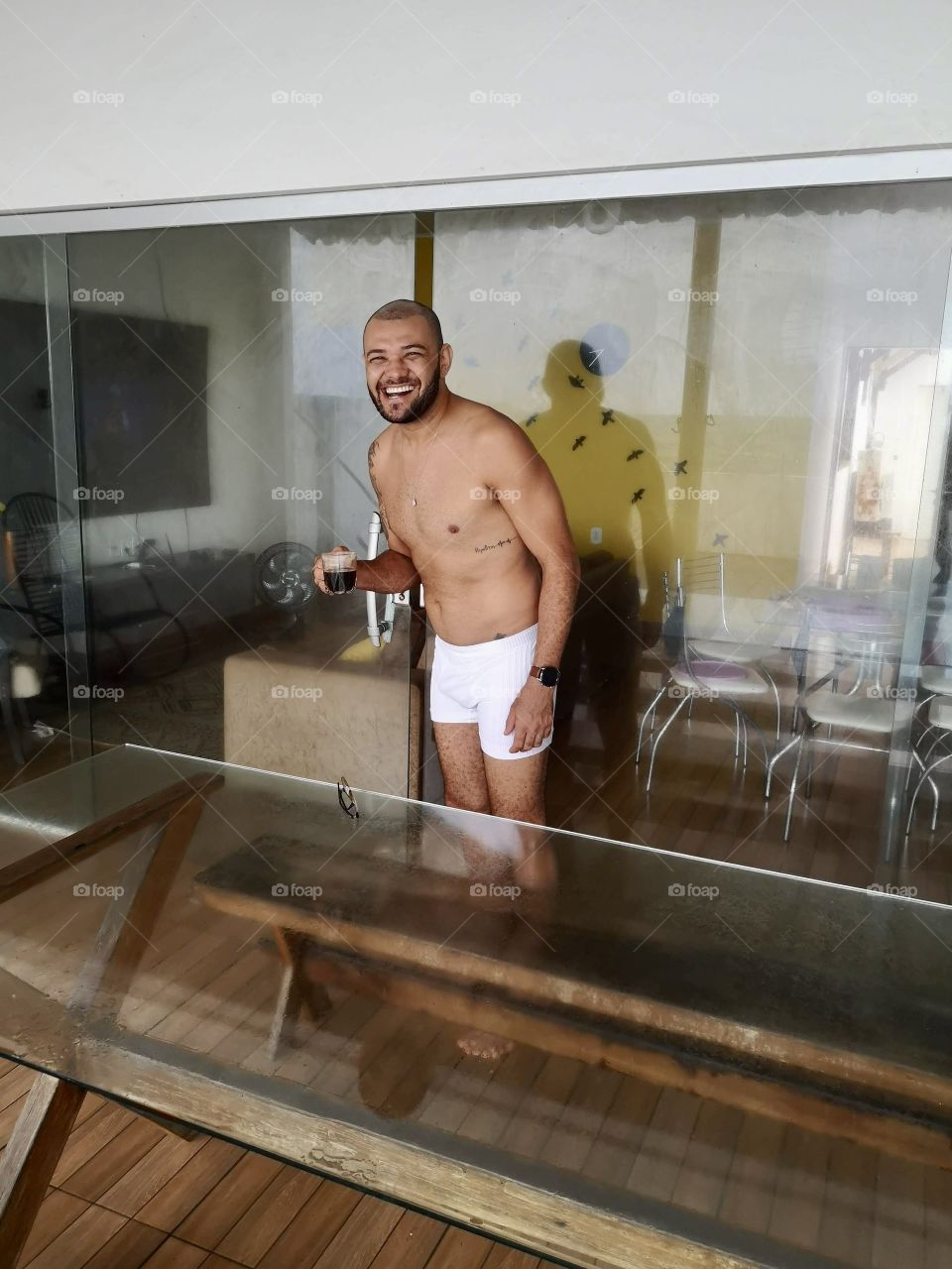 Man in a white swimsuit smiling with a cup of coffee in his hand