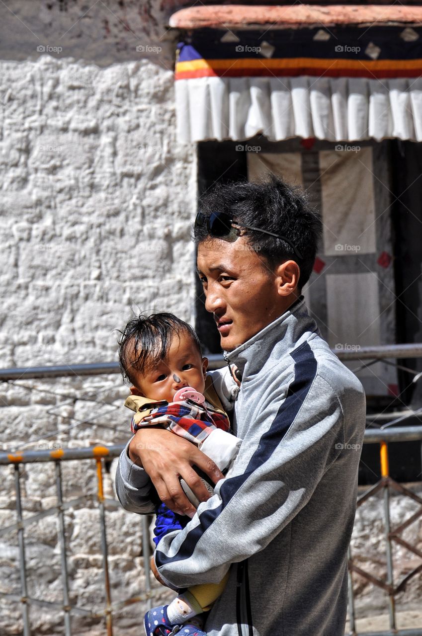 man holding cute baby in the buddhist monastery yard in tibet