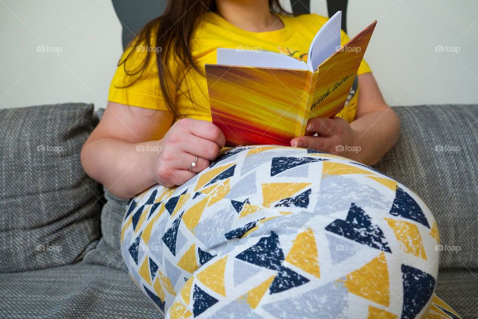 Young girl sitting on the couch and reading a book.