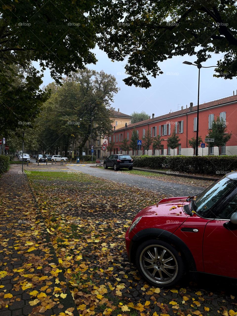 Autumn street in Italy, Parma, with bright red car and yellow leaves, peachy building in the background 