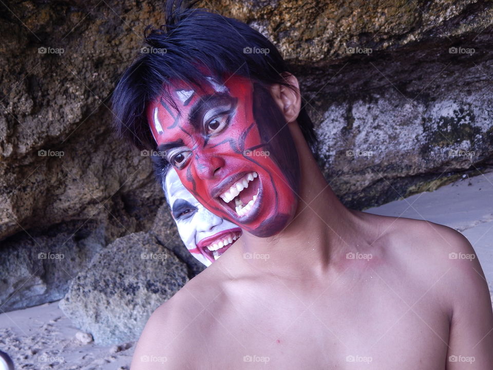 Teenager boy with painted face standing against rock