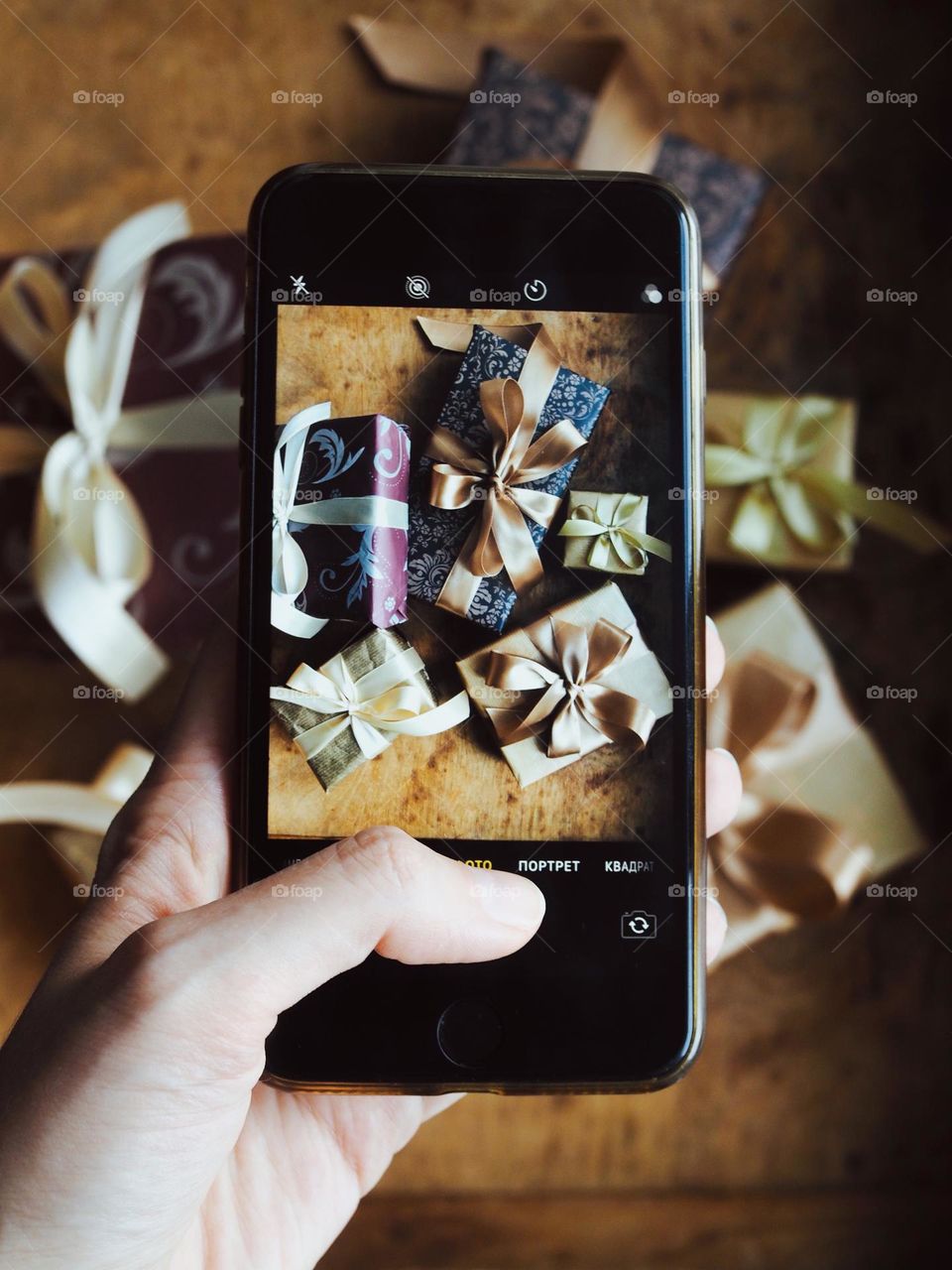 Female hand taking photo with smartphone of stylish wrapped Christmas gifts on wooden background. The girl taking a picture of a gifts on the phone. Christmas, New Year, social media, holiday concept, rectangle 