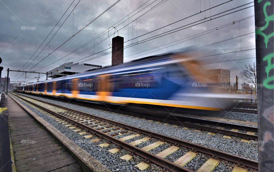 Blue and yellow NS Train passing by on high speed on the railroad in the center of Amersfoort the Netherlands long shuttertime dynamic picture