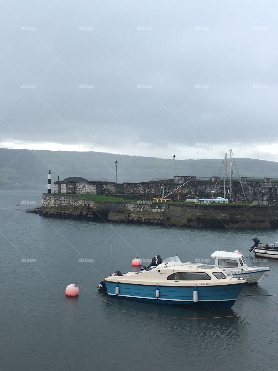A picture of some very small boats in a small marina in Ireland. It’s a cloudy and rainy day and there are some mountains in the distance 