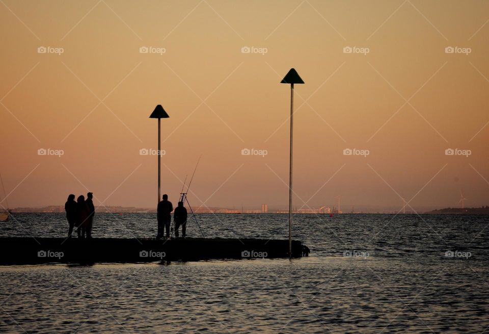 Sunset with silhouette of people fishing off a jetty 