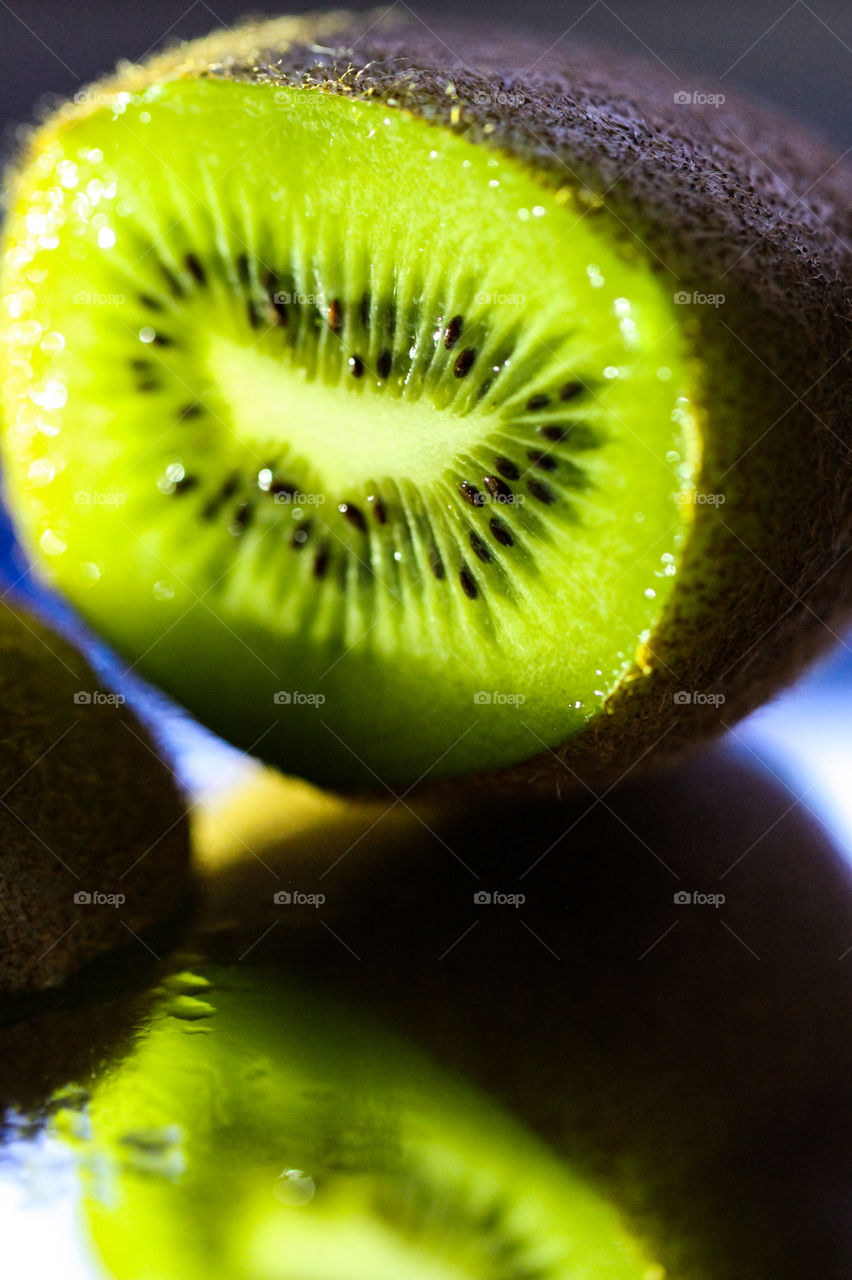 Macro of a cut ripe Kiwi fruit on a mirror. Kiwi is a berry because it is a single fleshy fruit without a stone & contains seeds. The Kiwi grows on a vine & is also called a Chinese gooseberry or the Chinese name of origin, mihoutau.