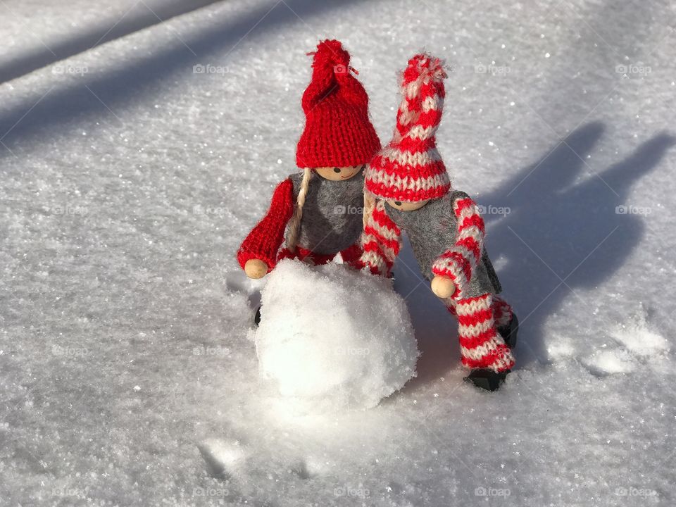 two small wooden man building a snowman made of snow, clear winter day