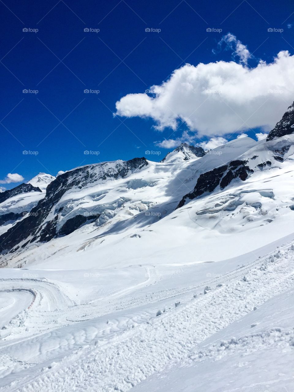 There is a lot of white snow on the top of the mountain , dark blue sky and big white cloud, day has many sunny but at here is very cold