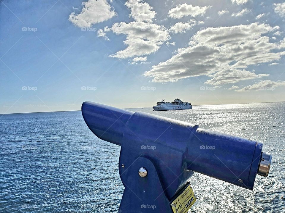 blue telescope, in the background the sea and a ferry