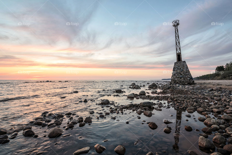 old lighthouse in rocky beach at sunset hour