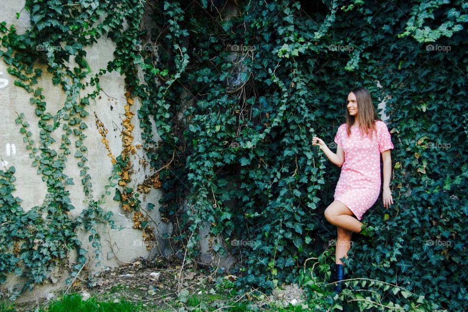 Woman in pink dress standing against poison ivy wall