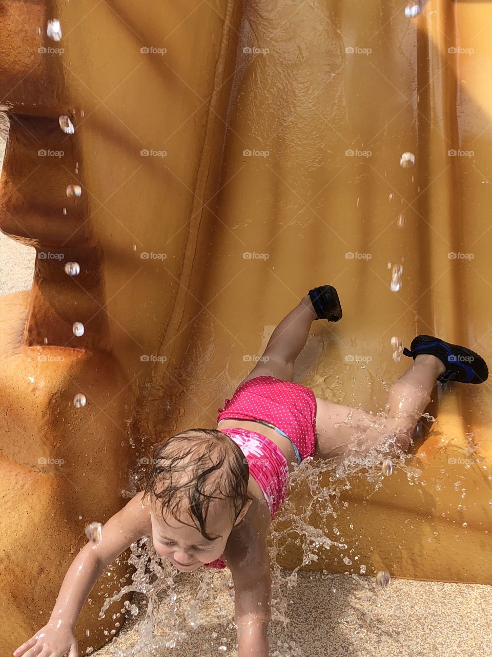Toddler girl going headfirst down a water slide 