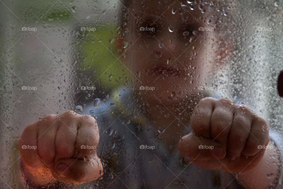 sad portrait of a boy through wet glass with drops