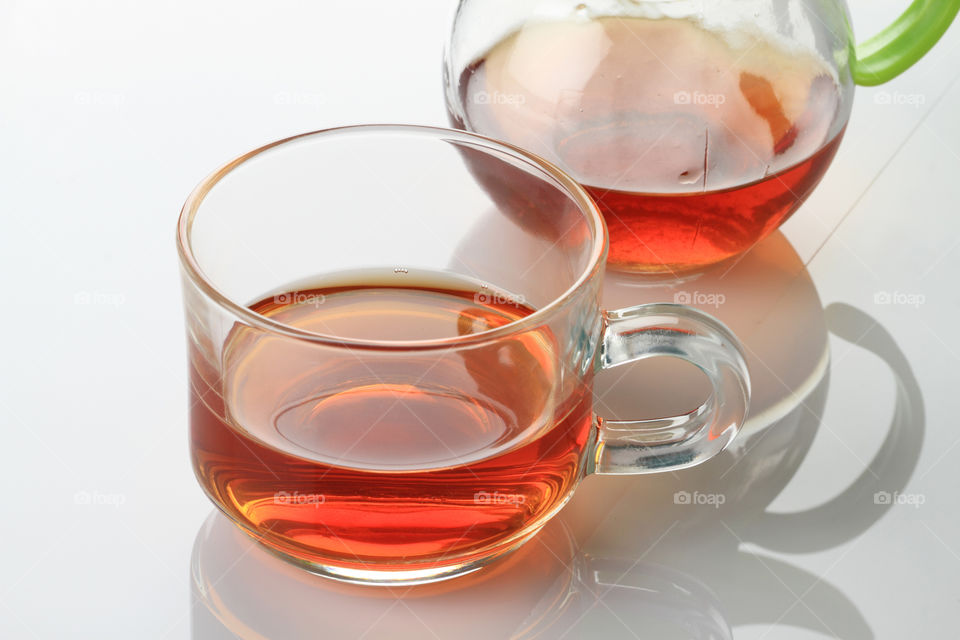 A cup of tea and kettle on white reflective background