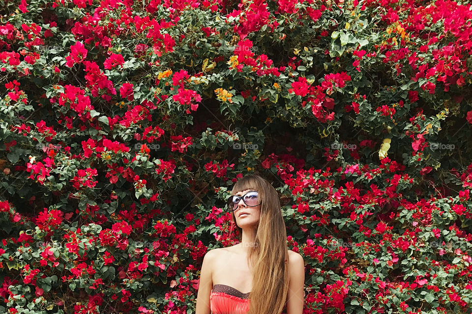 Young woman with long hair in front of pink flowering wall 