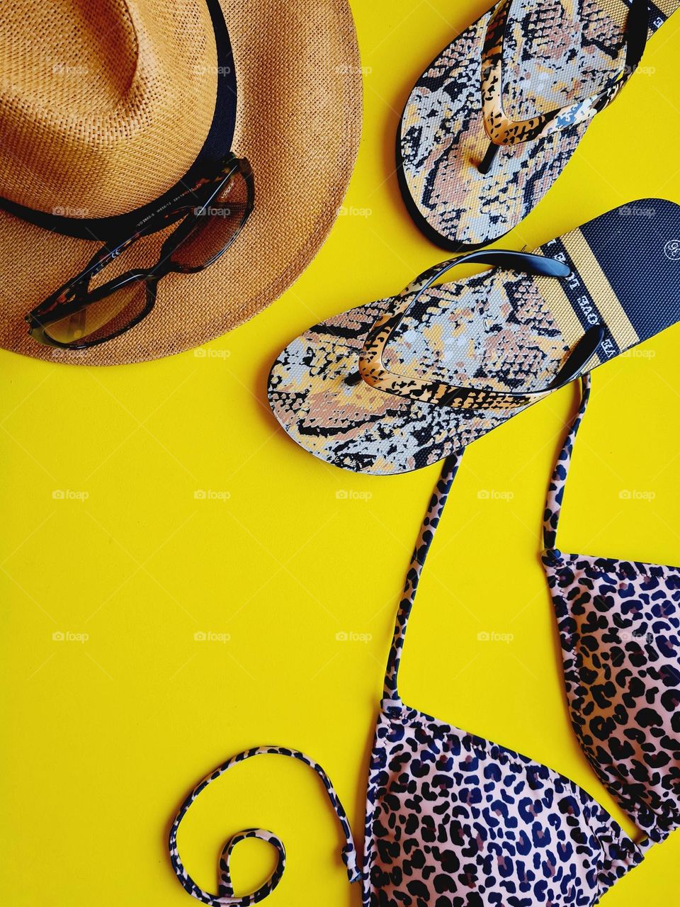 flat lay on a background with summer accessories: straw hat, bikini, sunglasses and flip flops