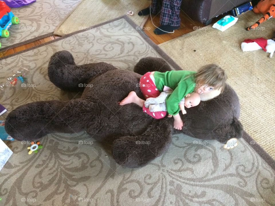 Child with Down syndrome laying on giant bear with doll