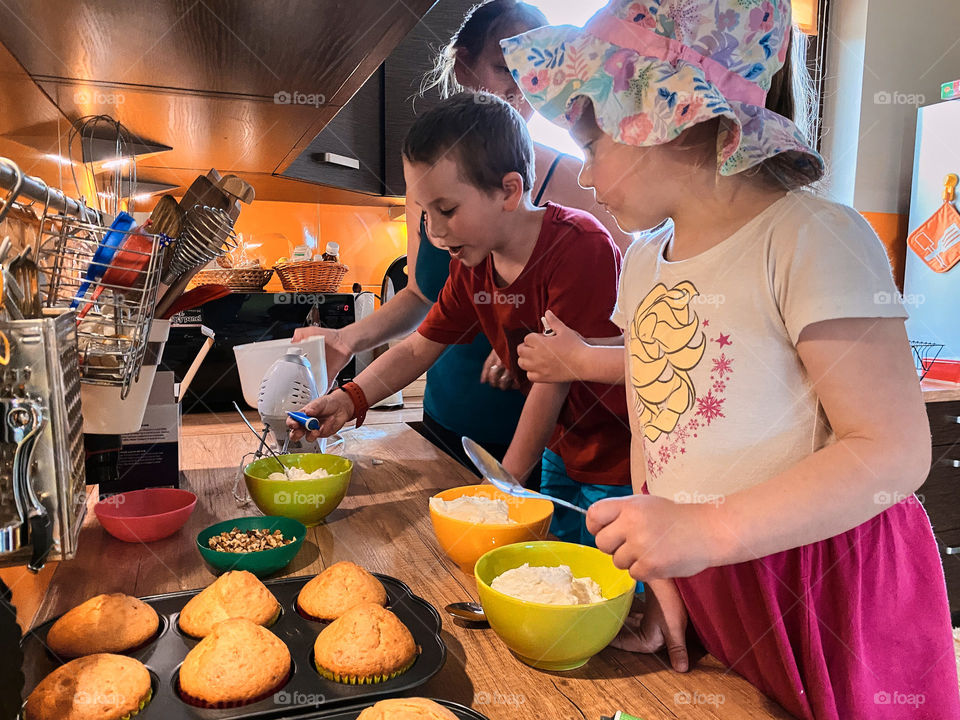 Group of children baking cupcakes, preparing ingredients, toppings, sprinkles for decorating cookies. Kids learning to cook, working together in kitchen at home. Concept of happy family