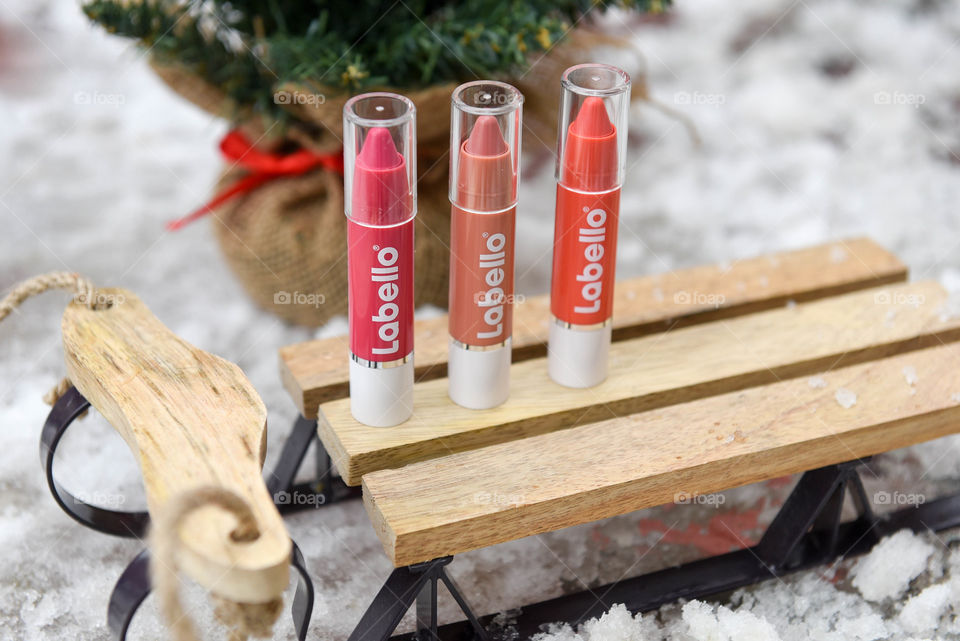 Row of Labello lip crayons standing on a mini wooden sled in the snow with a pine tree in the background