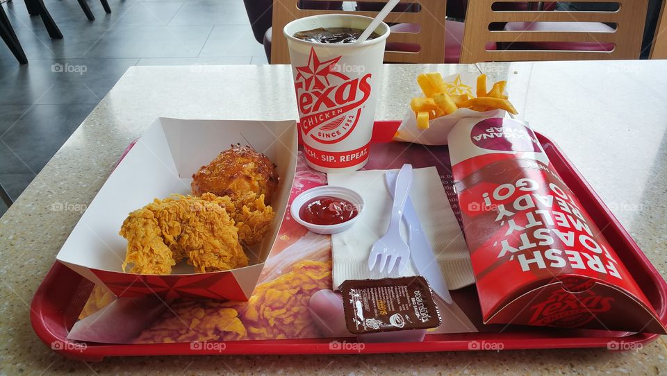 Texas Chicken on a tray at a restaurant in Bangkok, Thailand with a drink, french fries and chicken strips.