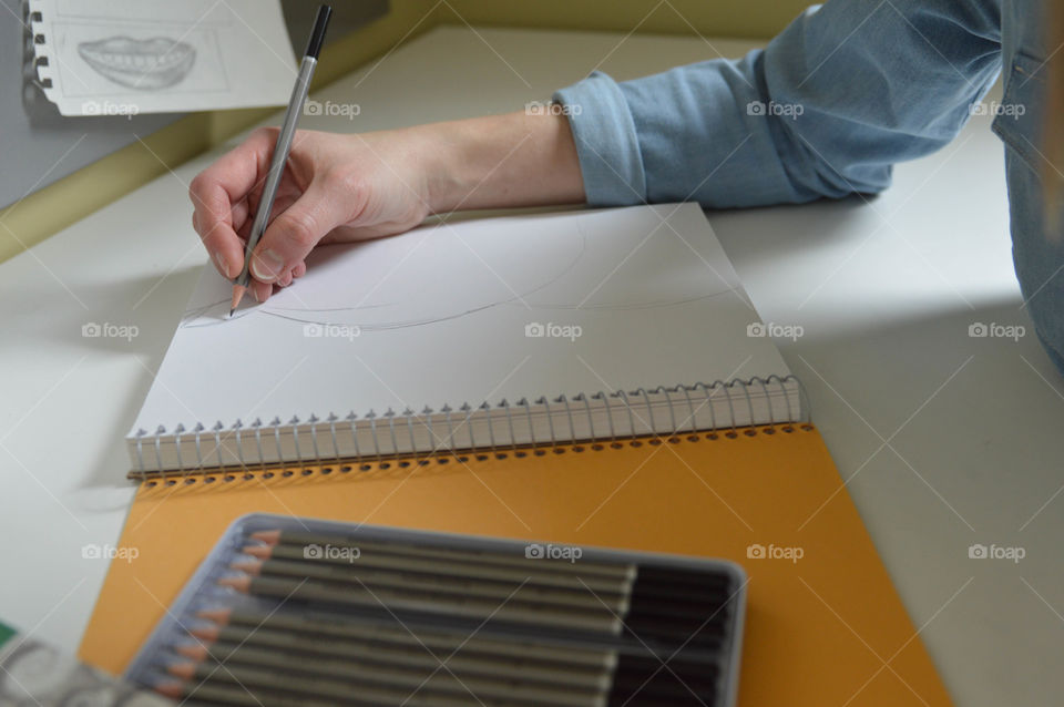 Woman drawing in a sketchbook with a pencil at a desk