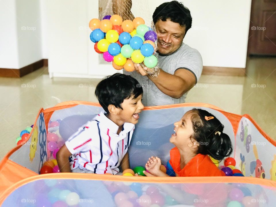 Kids having great fun with father and they enjoying a lot in ball pit by father pouring balls into pit