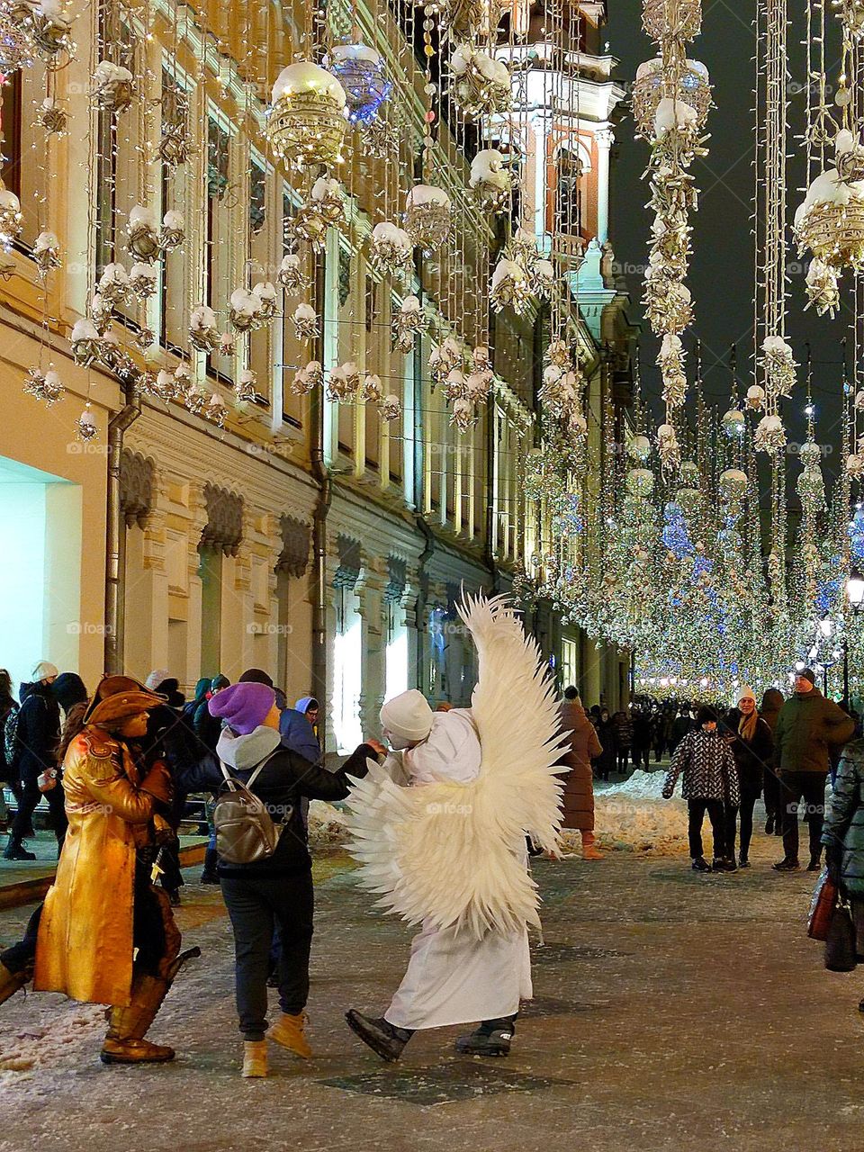 Happiness.  On a winter evening street that glows from burning garlands, a man dressed as a pirate and a man dressed as an angel are dancing with a girl.  Photo from which the beholder has a smile on his face and happy emotions