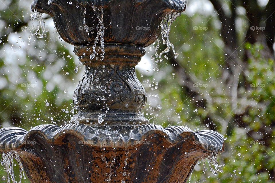 Liquids are cool - A stream of water droplets are dripping from a two tier bronze water fountain